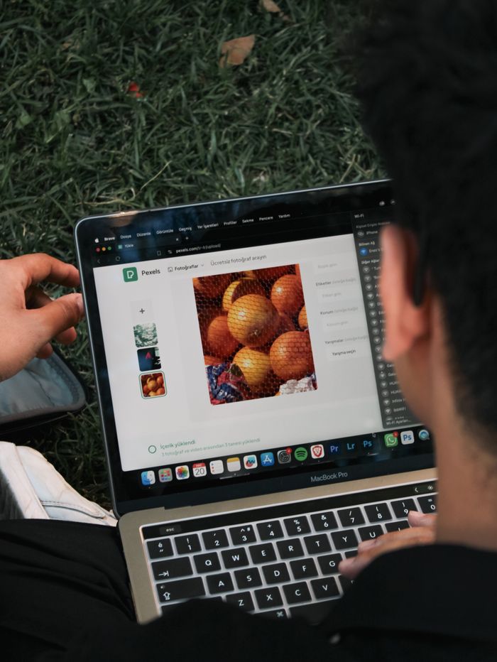 about-01 A man edits a fruit image on a MacBook Pro while sitting outdoors on grass.